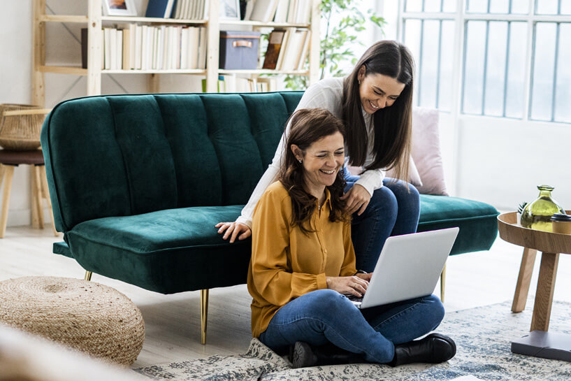 Dos mujeres sonríen mientras una trabaja en una laptop.