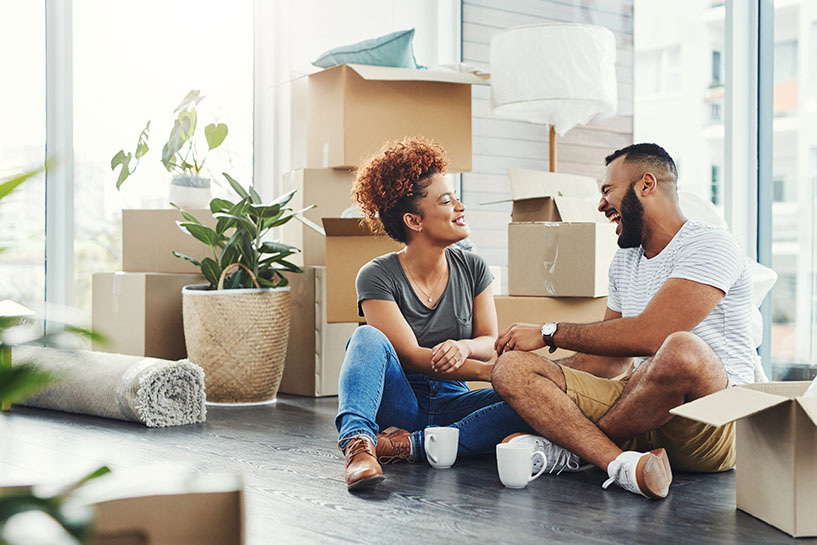 Two people sit and laugh next to open boxes in their new apartment.