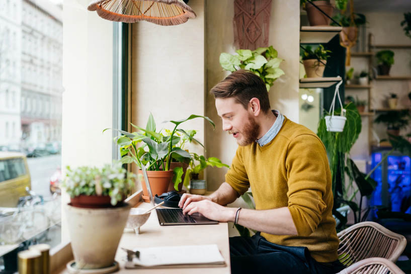 A man works at a laptop by a window overlooking a city street.