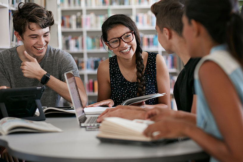 Estudiantes sentados en una mesa de la biblioteca sonriendo.