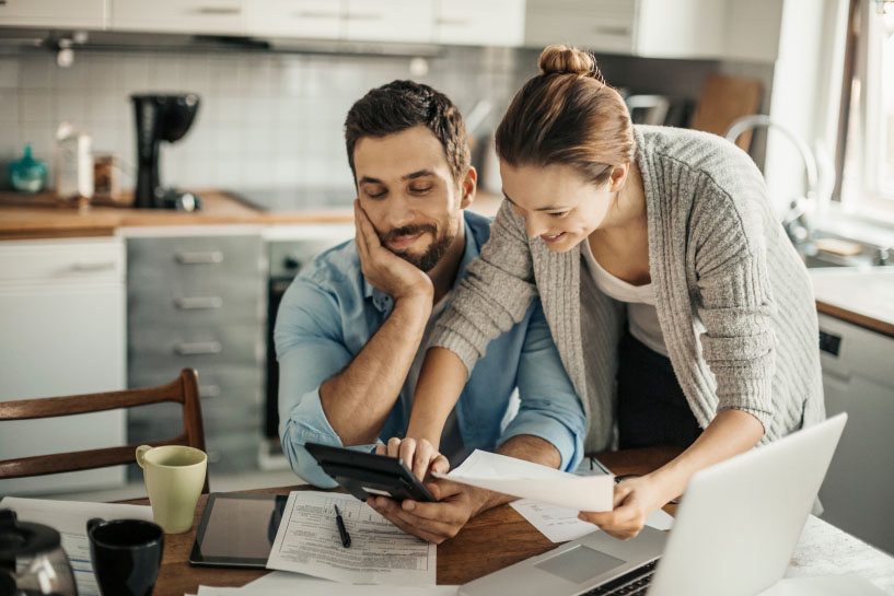 Dos personas trabajan con una laptop, páginas impresas, y un dispositivo móvil.